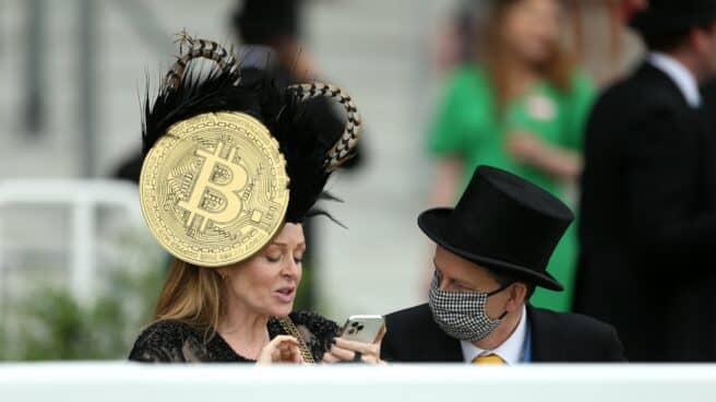 Una mujer, con una pamela con el símbolo del Bitcoin, en las carreras de caballos de Ascot.
