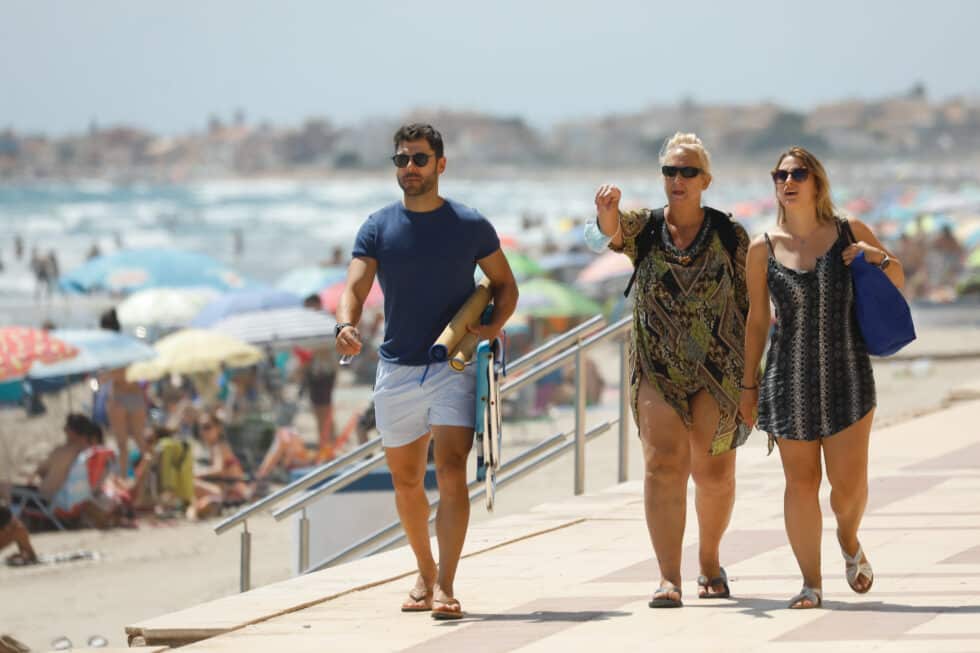 Tres personas caminan sin mascarilla, en el paseo marítimo de la playa de La Manga.