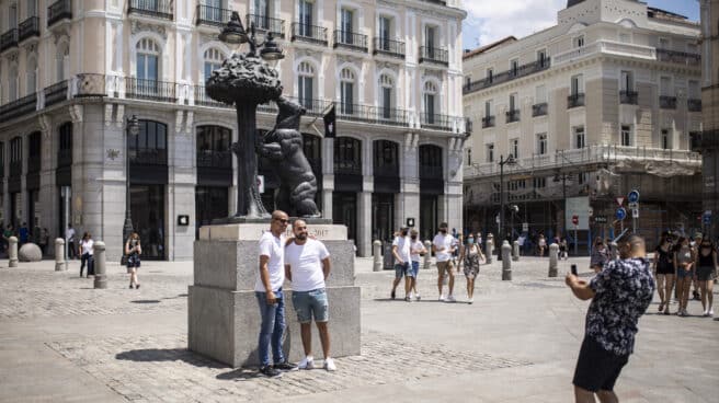 Un hombre toma una foto a otros dos, sin mascarilla en la Puerta del Sol.