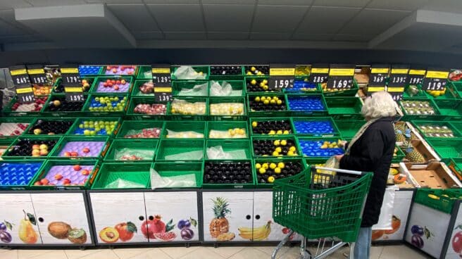 Un mujer coloca fruta en una bolsa mientras observar los productos que quedan en las cajas de un supermercado.