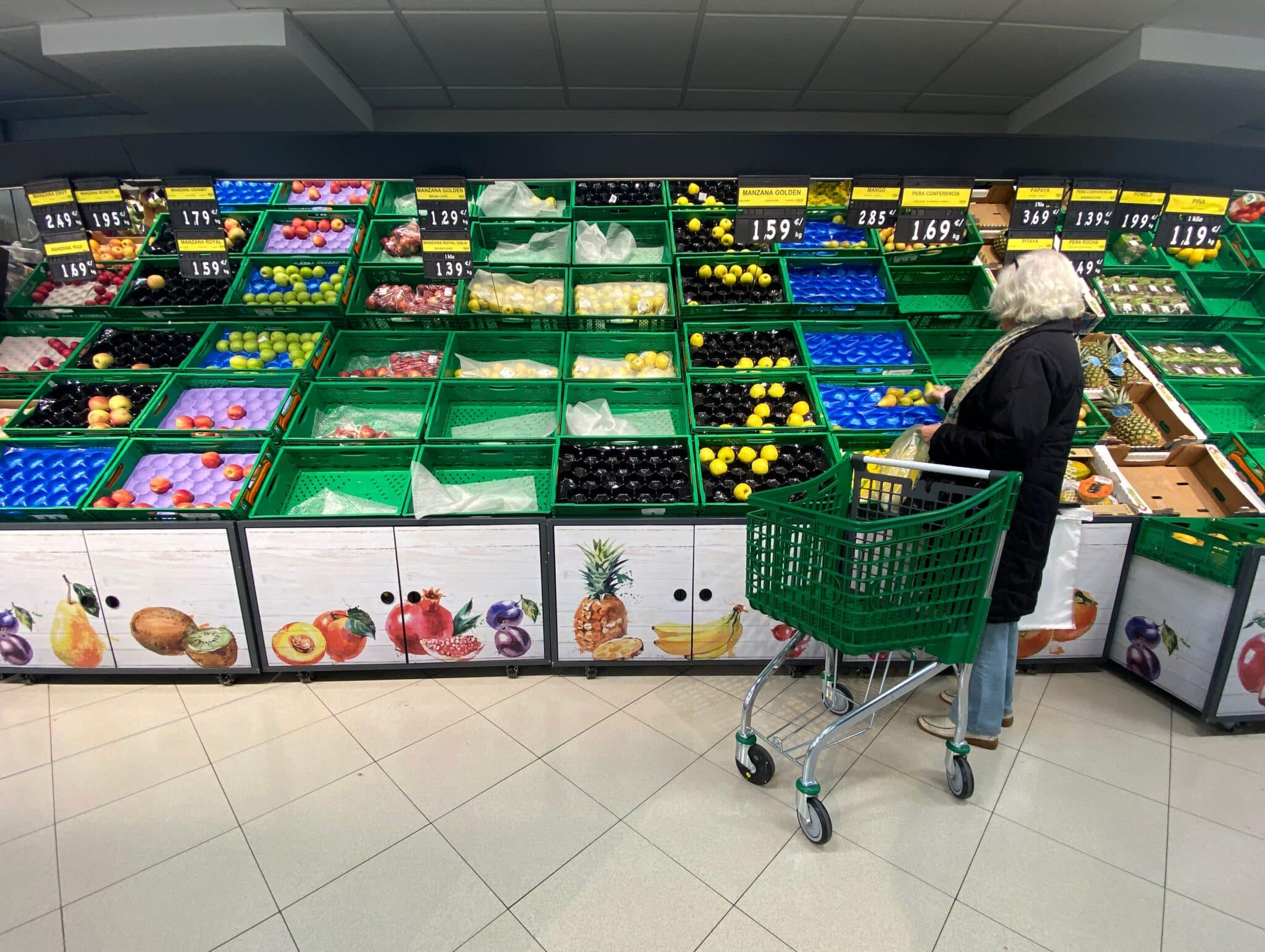 Un mujer coloca fruta en una bolsa mientras observar los productos que quedan en las cajas de un supermercado.