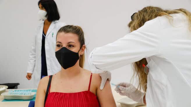 Mujer joven con mascarilla recibiendo una vacuna contra el coronavirus con una sanitaria inyectándole la vacuna