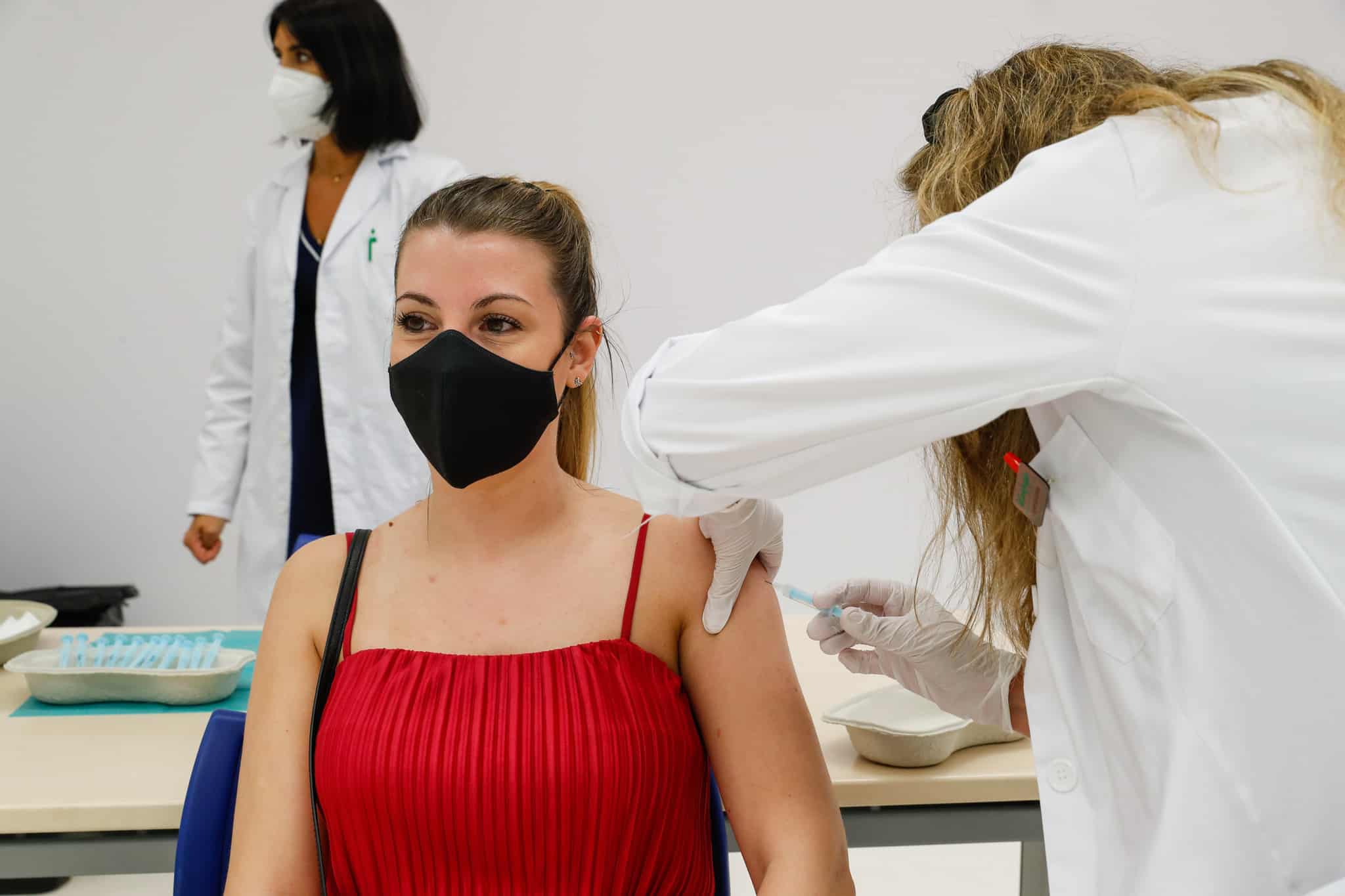 Mujer joven con mascarilla recibiendo una vacuna contra el coronavirus con una sanitaria inyectándole la vacuna