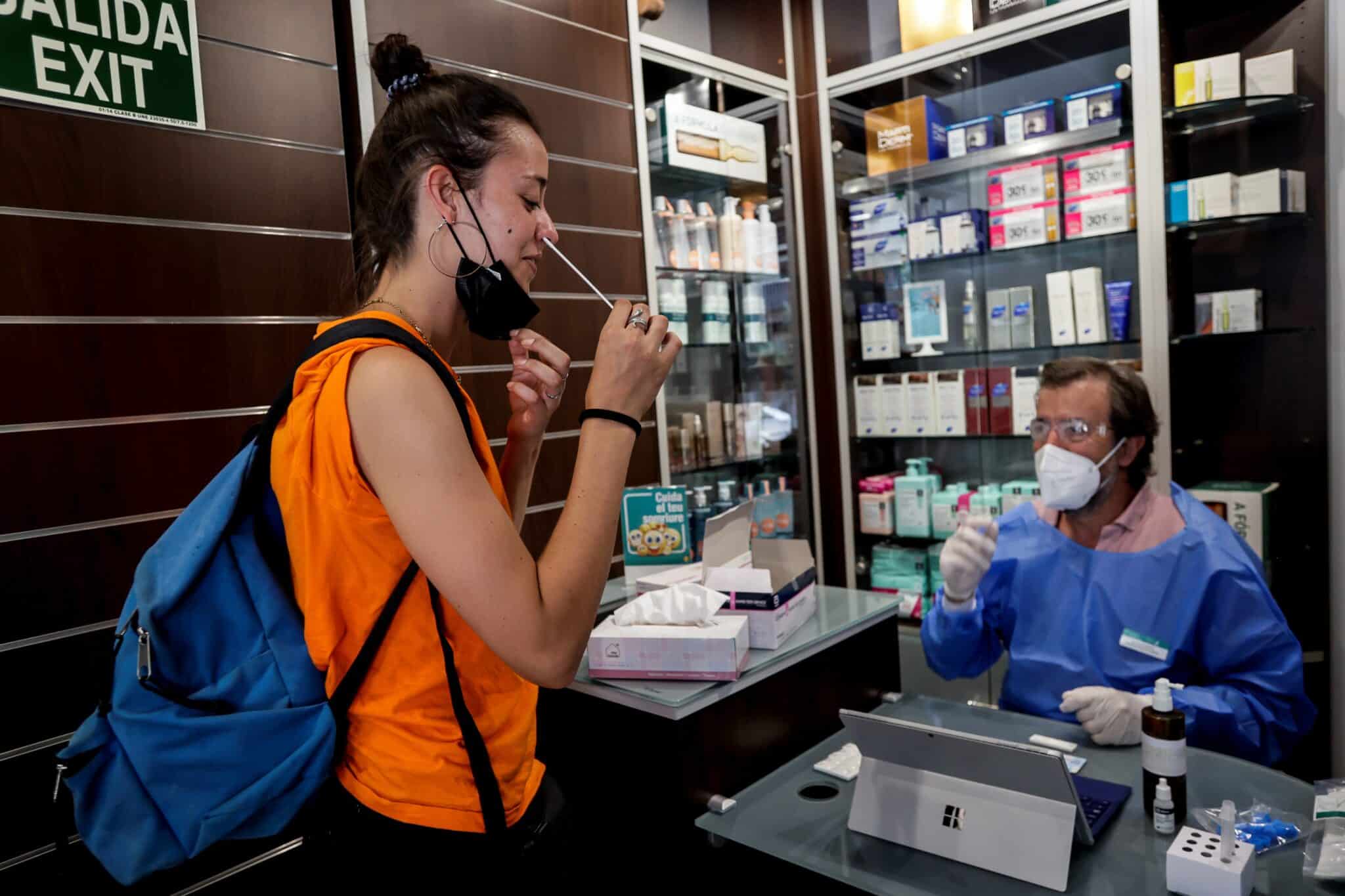Chica realizándose un test de antígenos de autodiagnóstico en una farmacia junto a un farmacéutico