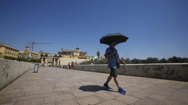 Un hombre se resguarda del sol bajo un paraguas mientras camina por el Puente Romano de Córdoba.