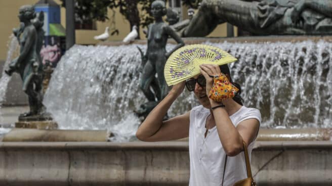 Una mujer se tapa la cabeza con un abanico para guarecerse de las altas temperaturas en Valencia.