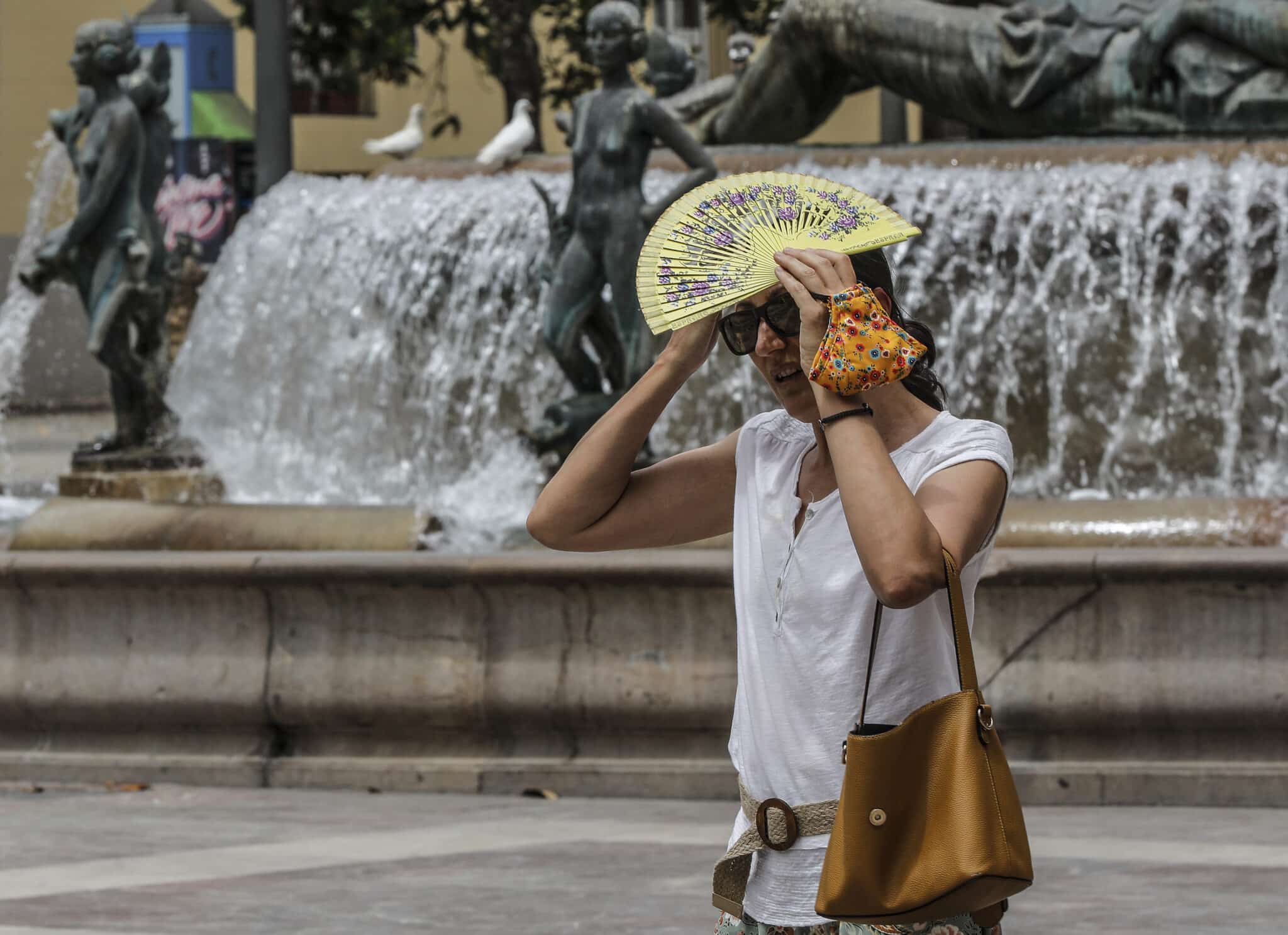 Una mujer se tapa la cabeza con un abanico para guarecerse de las altas temperaturas en Valencia.
