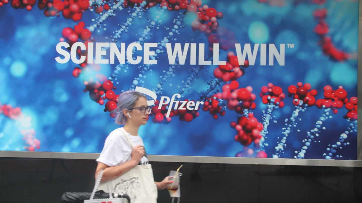 Una mujer camina por Nueva York delante de un anuncio de Pfizer con el eslogan "La ciencia ganará".