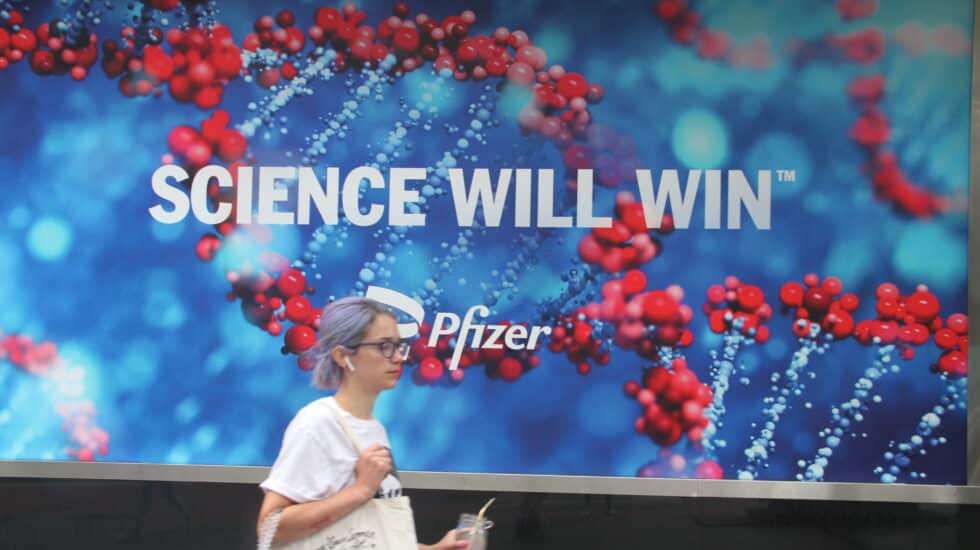Una mujer camina por Nueva York delante de un anuncio de Pfizer con el eslogan "La ciencia ganará".