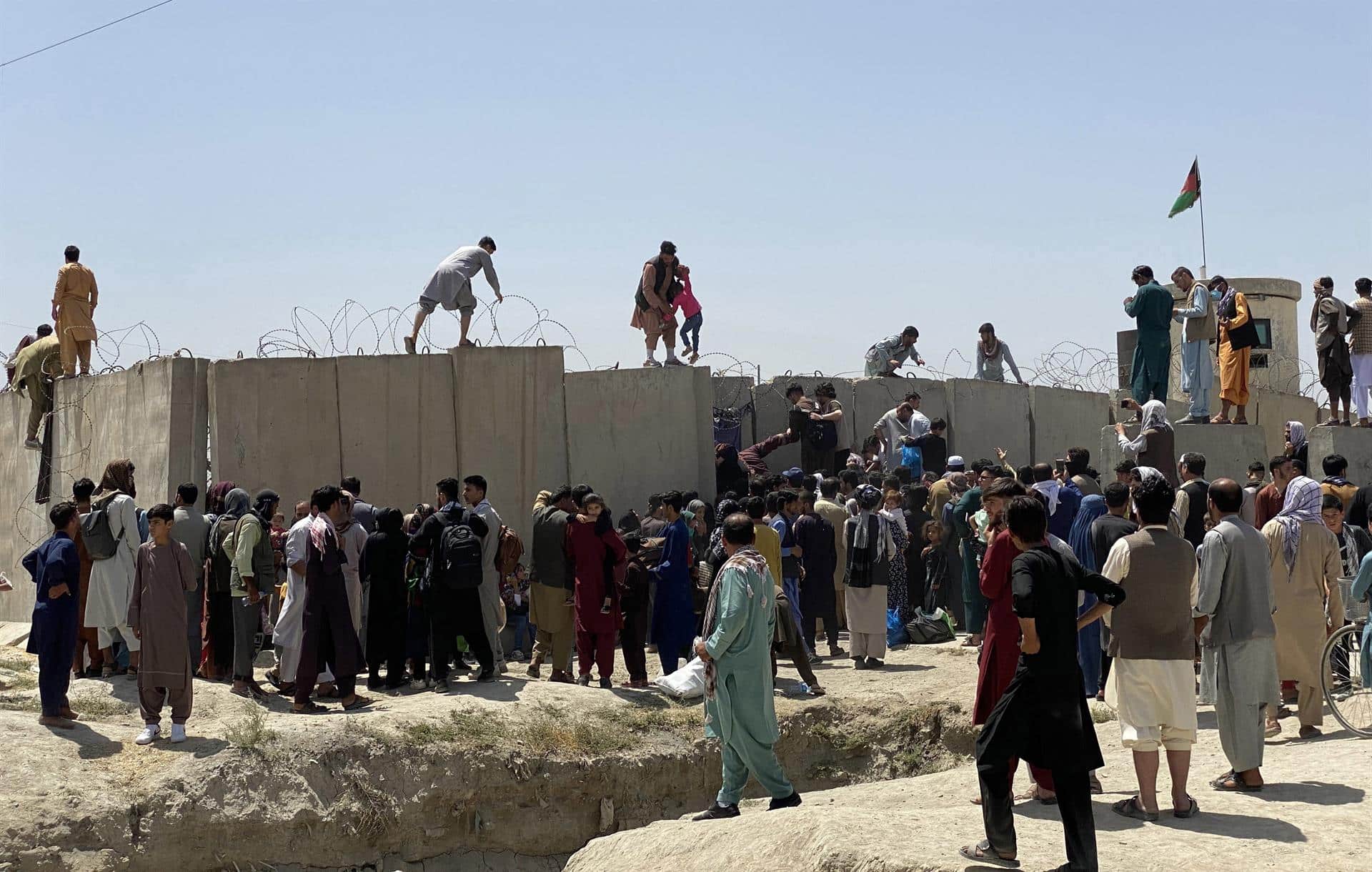 Afganos se agolpan a lo largo del muro del aeropuerto internacional Hamid Karzai antes de saltarlo en un intento de abandonar el país, este lunes en Kabul, después de darse a conocer de que el propio presidente afgano, Ashra Ghani, huyera ayer en secreto