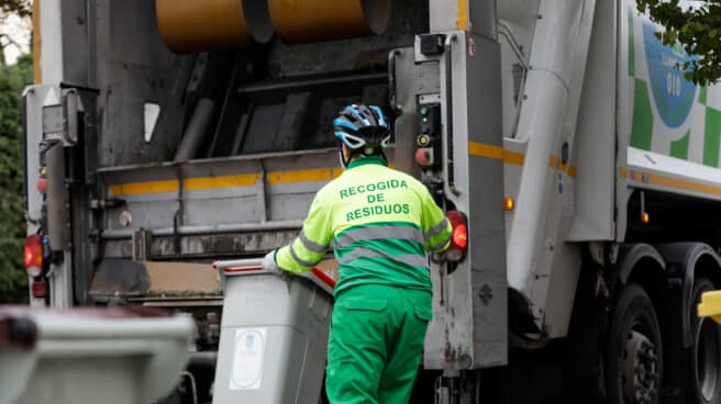 Un operario de recogida de residuos protegido con mascarilla se dispone a colocar un cubo de basura en la trituradora de desechos Un operario de recogida de residuos protegido con mascarilla se dispone a colocar un cubo de basura en la trituradora de desechos .