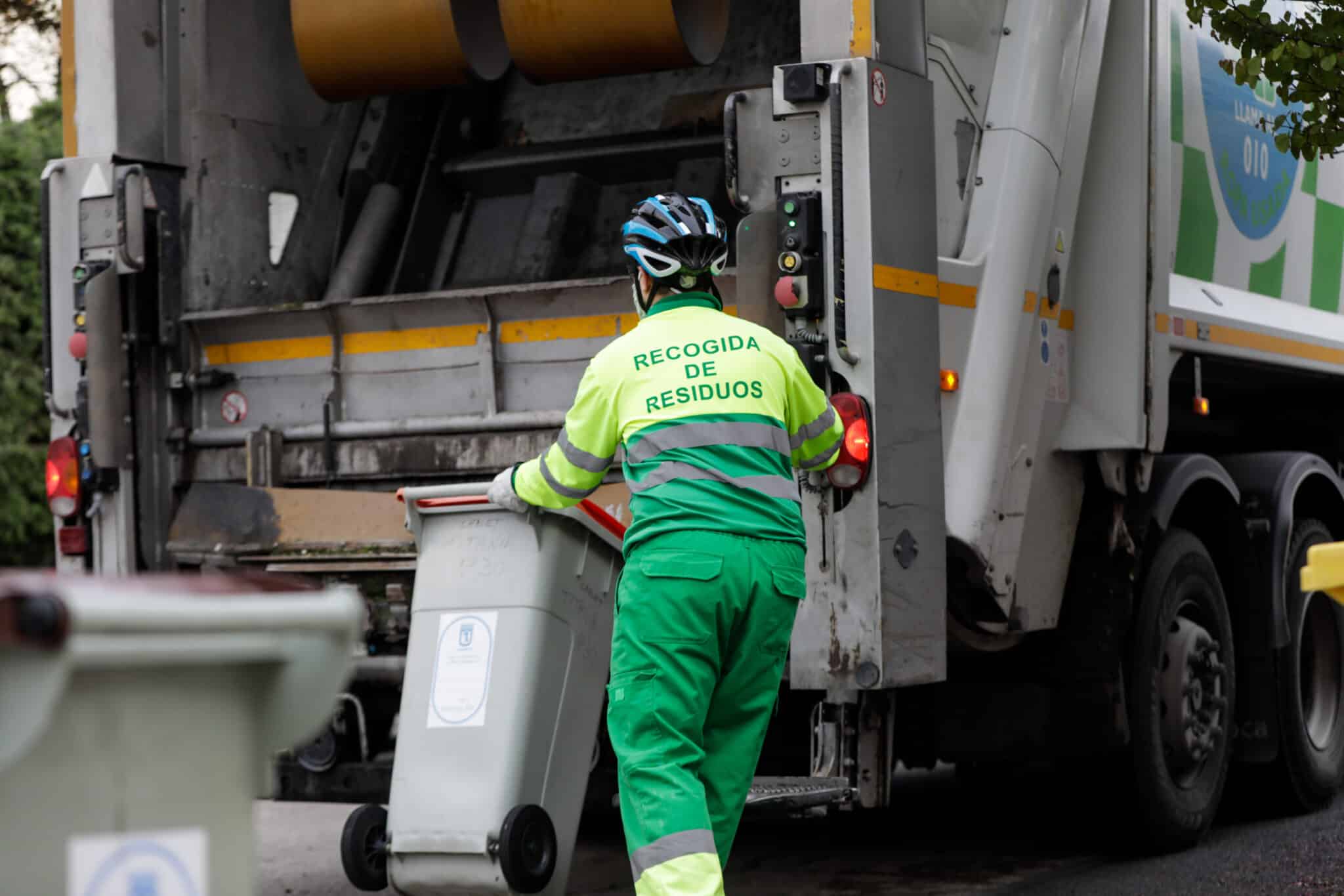 Un operario de recogida de residuos protegido con mascarilla se dispone a colocar un cubo de basura en la trituradora de desechos Un operario de recogida de residuos protegido con mascarilla se dispone a colocar un cubo de basura en la trituradora de desechos .