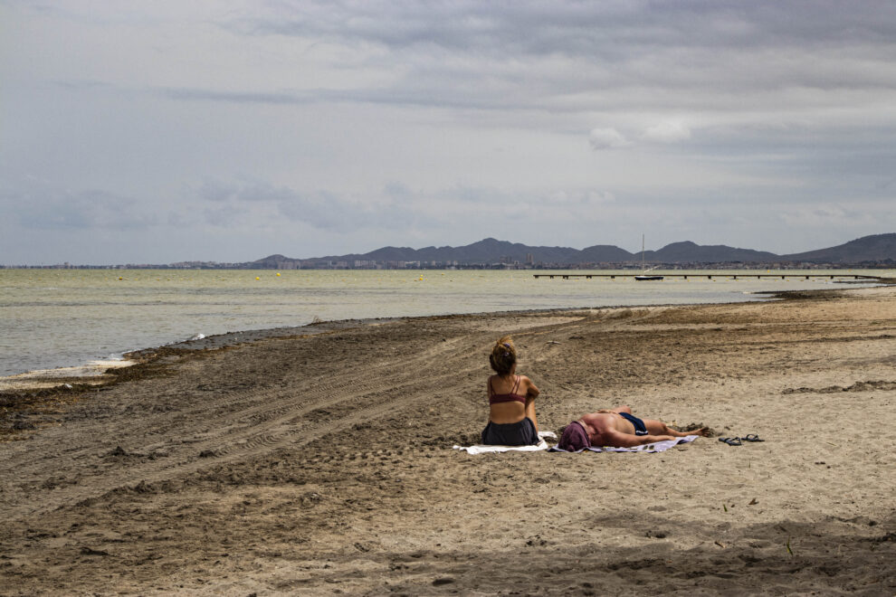 Dos bañistas toman el sol en la playa de Los Urrutias.