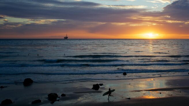 Un surfista en la orilla de una playa en la puesta de sol.