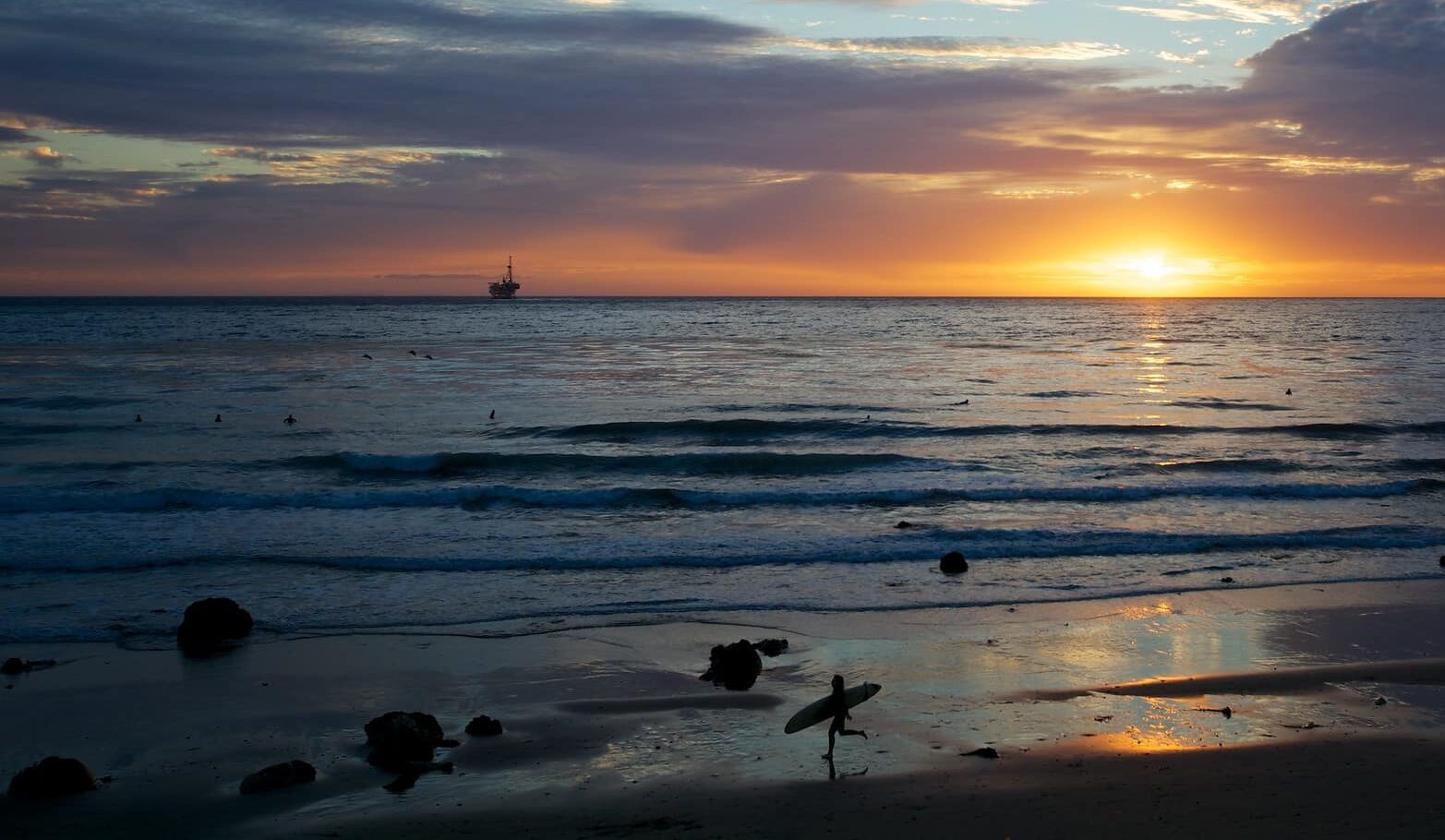 Un surfista en la orilla de una playa en la puesta de sol.