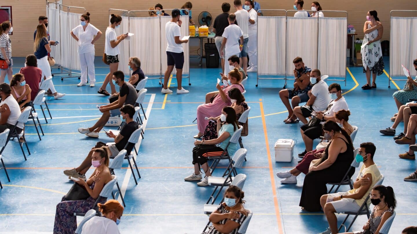 Multitud de jóvenes aguardan sentados tras recibir la vacuna contra el coronavirus, en el pabellón municipal de Espartinas (Sevilla).