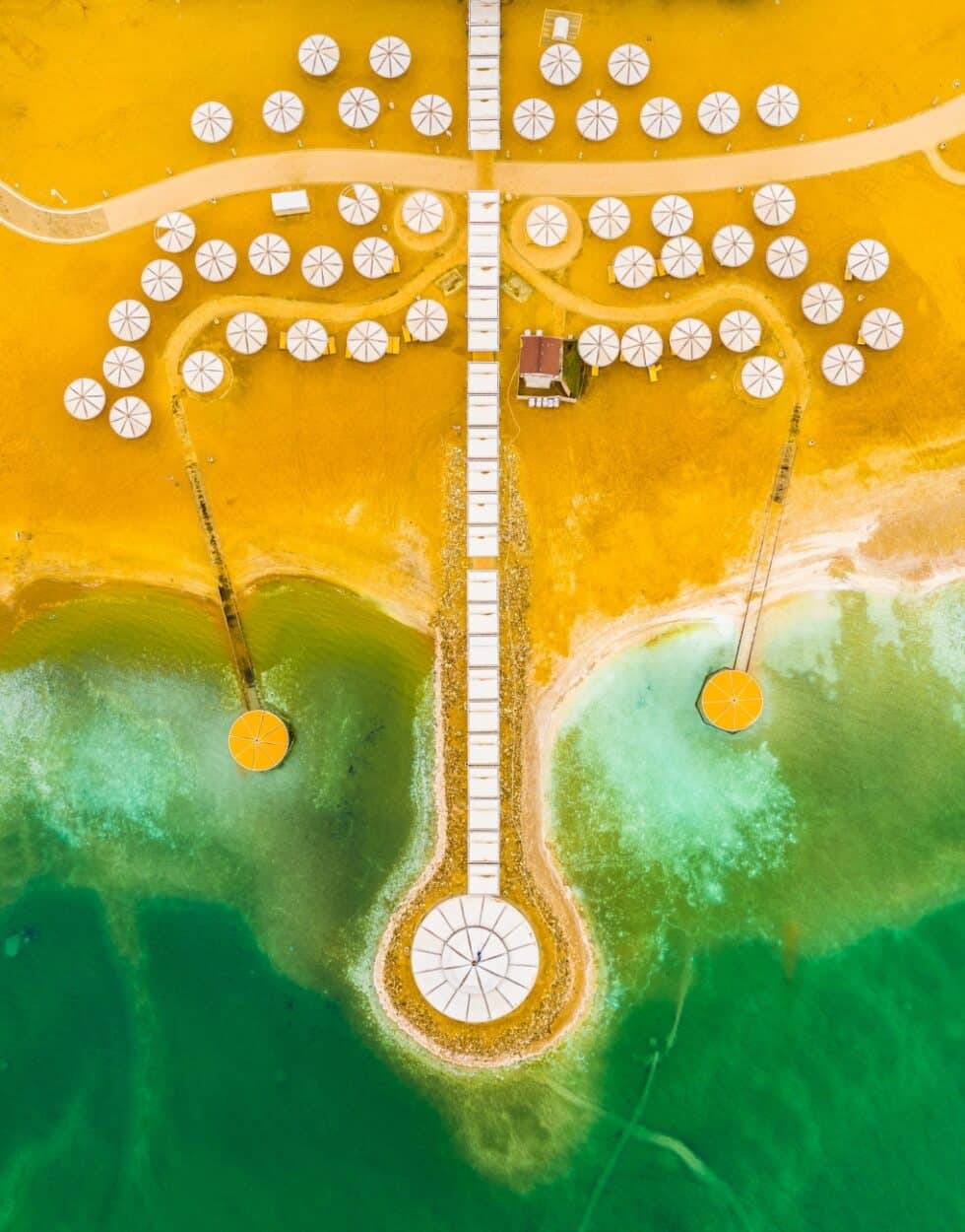Imagen de dron de una playa con sombrillas en colores amarillo y verde