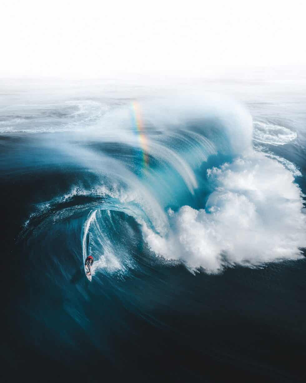 Imagen de un surfista en una ola gigante de Australia en la que aparece un arcoíris