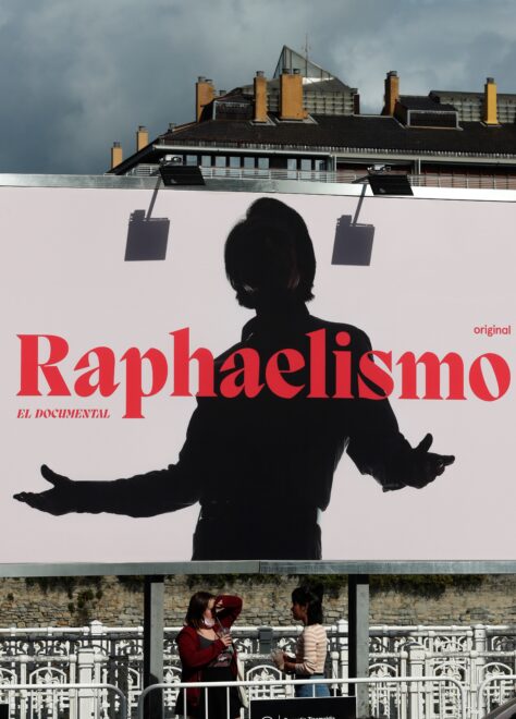 Dos jóvenes conversan bajo el cartel que anuncia el documental del cantante Raphael.