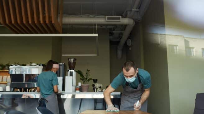 portrait-of-young-man-wearing-mask-while-cleaning-tables-with-sanitizer-at-cafe-or-coffee-shop-covid-safety-measures-copy-space
