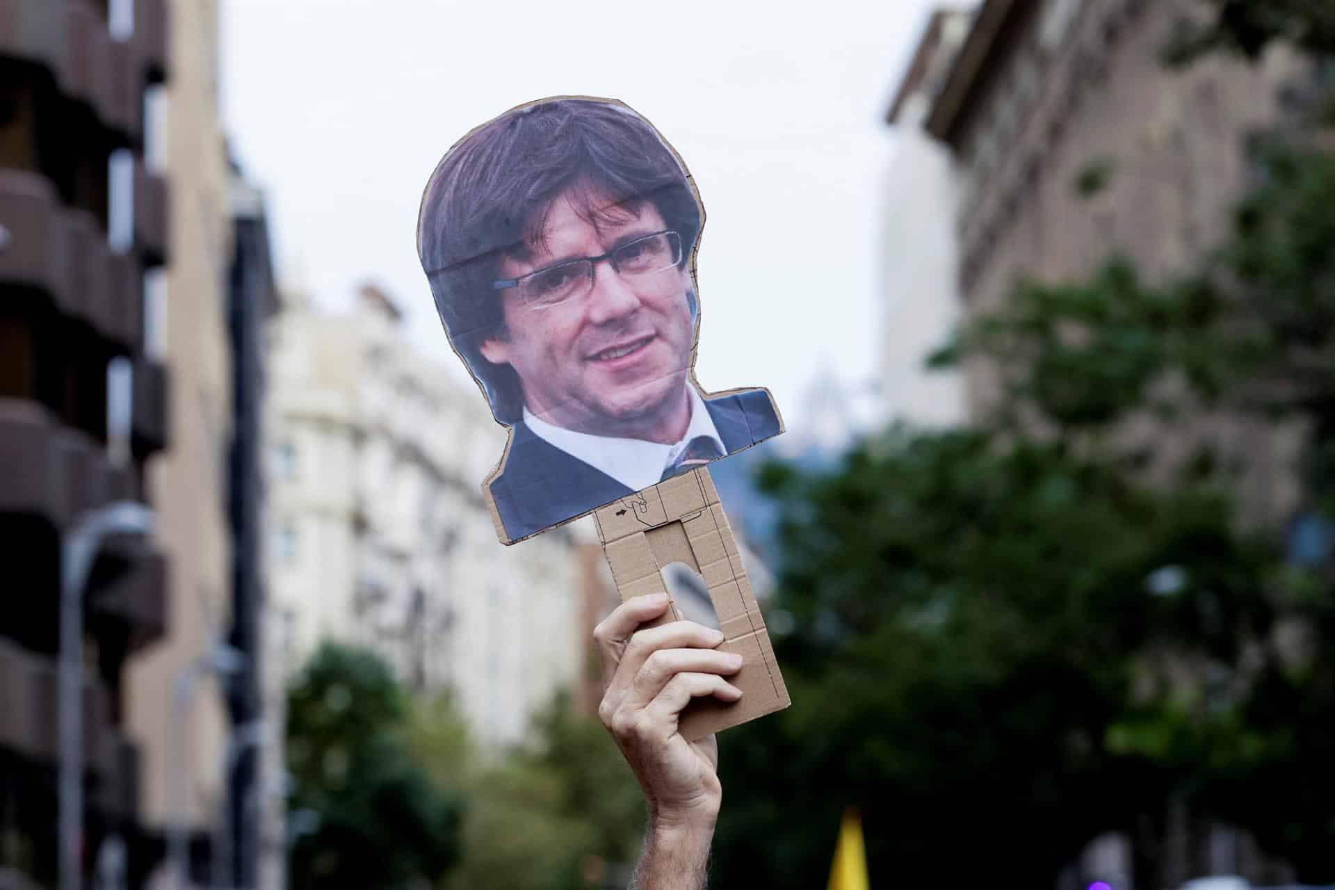 Una mano levanta una careta de Carles Puigdemont durante una manifestación en Barcelona.