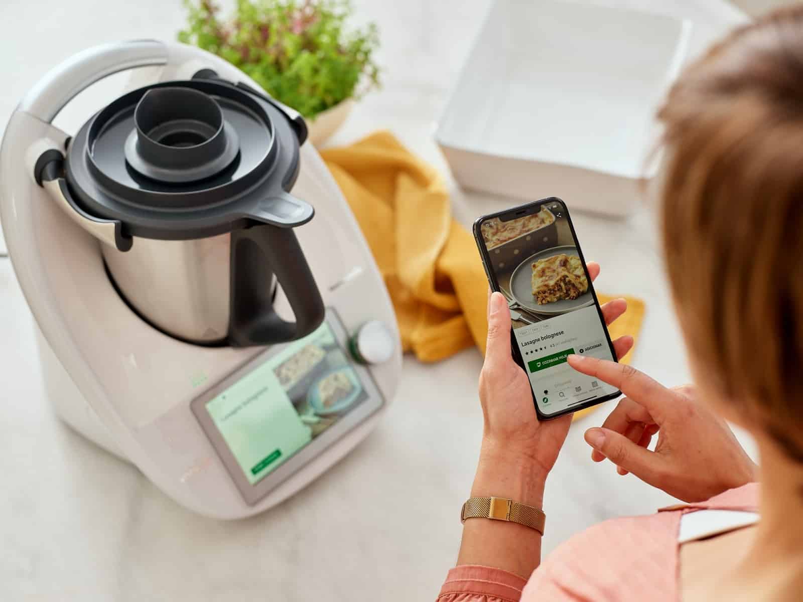 Imagen de una mujer con su teléfono móvil y una Thermomix.