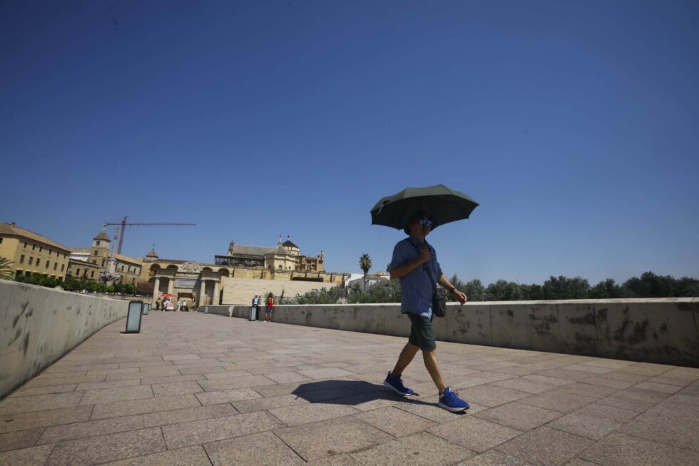 Un hombre se resguarda del sol bajo un paraguas mientras camina por el Puente Romano de Córdoba.