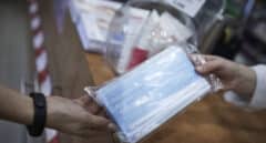 Una farmacéutica enseña a un cliente un paquete de mascarillas en la farmacia.
