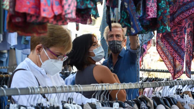 Varias personas visitan un puesto de ropa en El Rastro