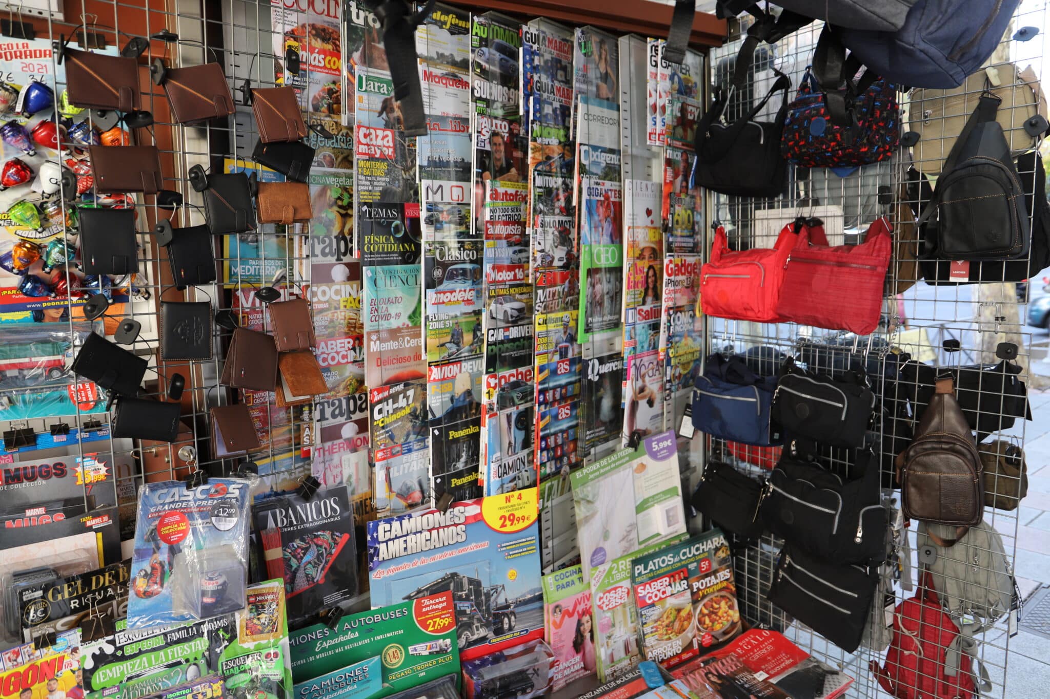 Productos como carteras y bandoleras se venden entre revistas y periódicos.