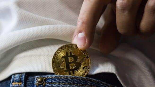 Una persona mete una moneda de bitcoin en el bolsillo de un pantalón