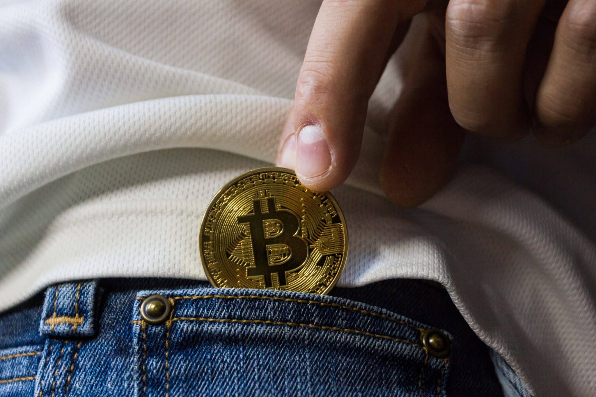 Una persona mete una moneda de bitcoin en el bolsillo de un pantalón