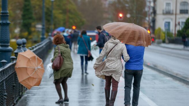 Personas andando bajo paraguas por un puente debajo de la lluvia y ráfagas de viento