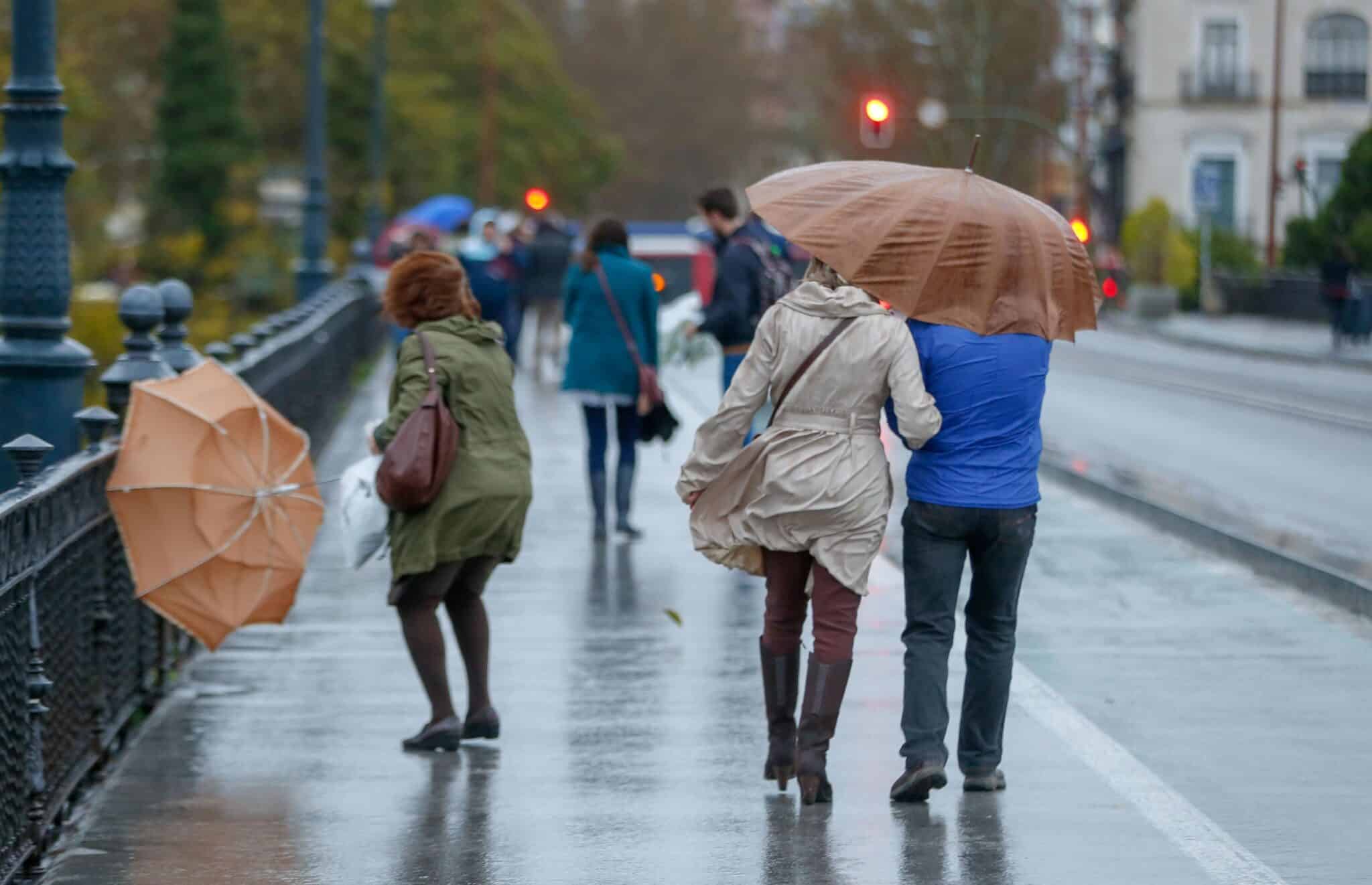 Personas andando bajo paraguas por un puente debajo de la lluvia y ráfagas de viento