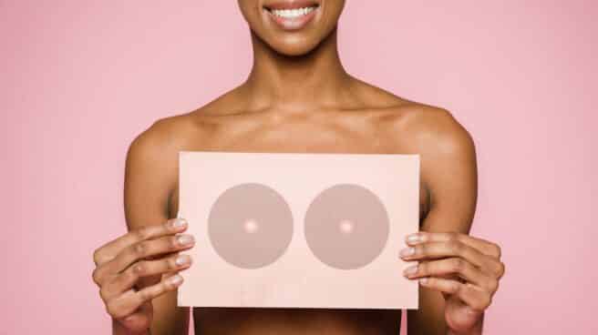 Imagen de archivo de una chica con el torso desnudo sosteniendo un cartel en el pecho rosa y sobre fondo rosa como representación d ela prevención del cáncer de mama