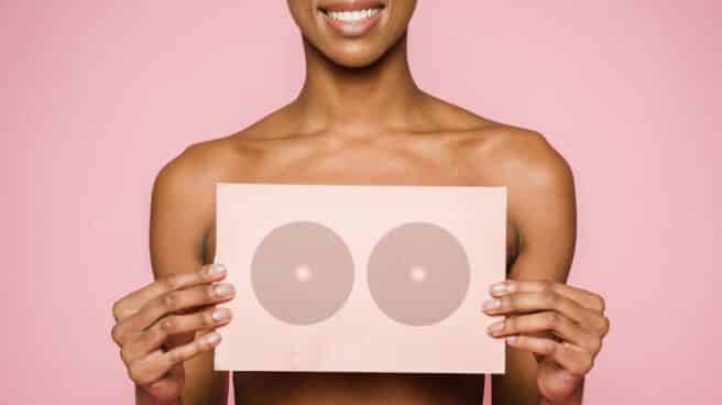 Cancer de mama o mastitis, conocer las enfermedades de la mama para prevenir el cancer Imagen de archivo de una chica con el torso desnudo sosteniendo un cartel en el pecho rosa y sobre fondo rosa como representación d ela prevención del cáncer de mama