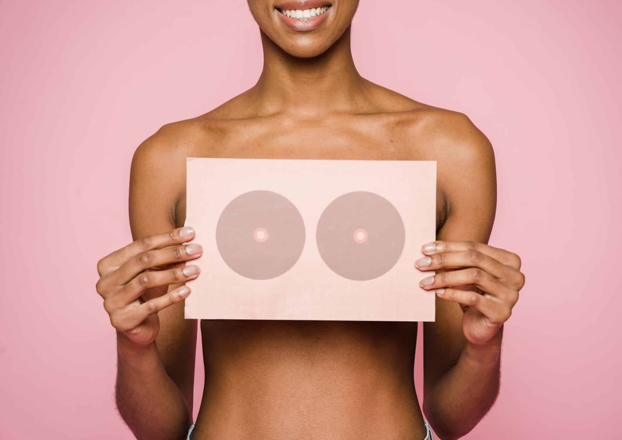 Imagen de archivo de una chica con el torso desnudo sosteniendo un cartel en el pecho rosa y sobre fondo rosa como representación d ela prevención del cáncer de mama