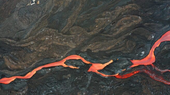 El tejado de una vivienda sobresale de la lava ya solidificada junto a una rio de magma que discurre por la fajana creada por la erupción del volcán Cumbre Vieja. La sismicidad asociada al volcán ha aumentado en las últimas horas en los niveles profundos a más de 20 kilómetros bajo tierra