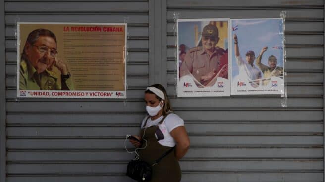 Una joven consulta su móvil junto a unos retratos de Miguel Díaz-Canel y Raúl Castro