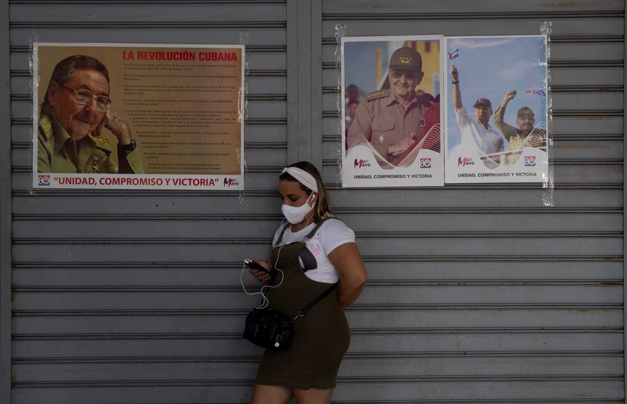 Una joven consulta su móvil junto a unos retratos de Miguel Díaz-Canel y Raúl Castro