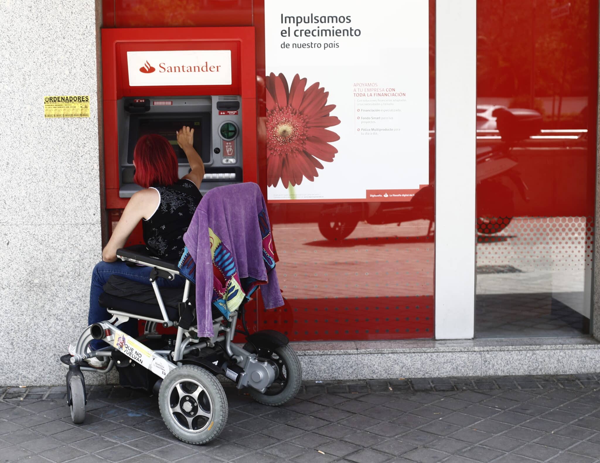 Una mujer en silla de ruedas saca dinero en un cajero del Banco Santander en Madrid.