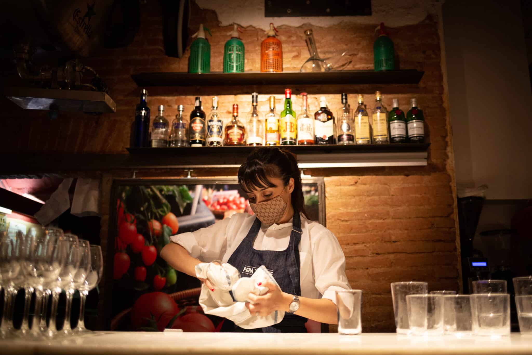 Una camarera seca unos vasos en el interior de un bar en una calle céntrica de Barcelona.