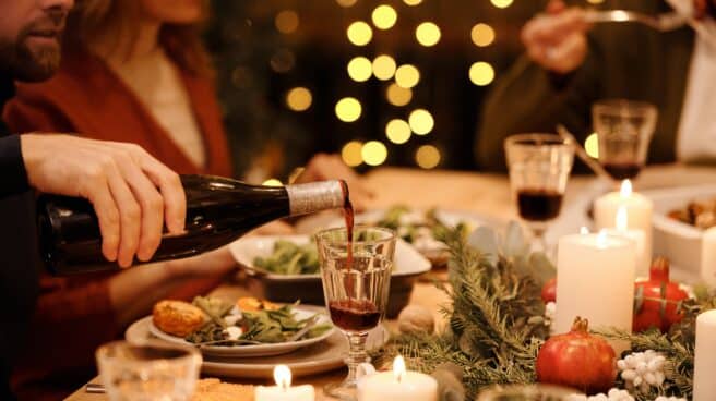 Una mano sirve una copa de vino en una mesa de Navidad, con velas y ramas.