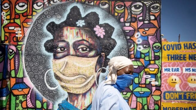 Una residente del barrio de Soweto en Johannesburgo, Sudáfrica, pasa delante de un mural que representa a una mujer con una mascarilla