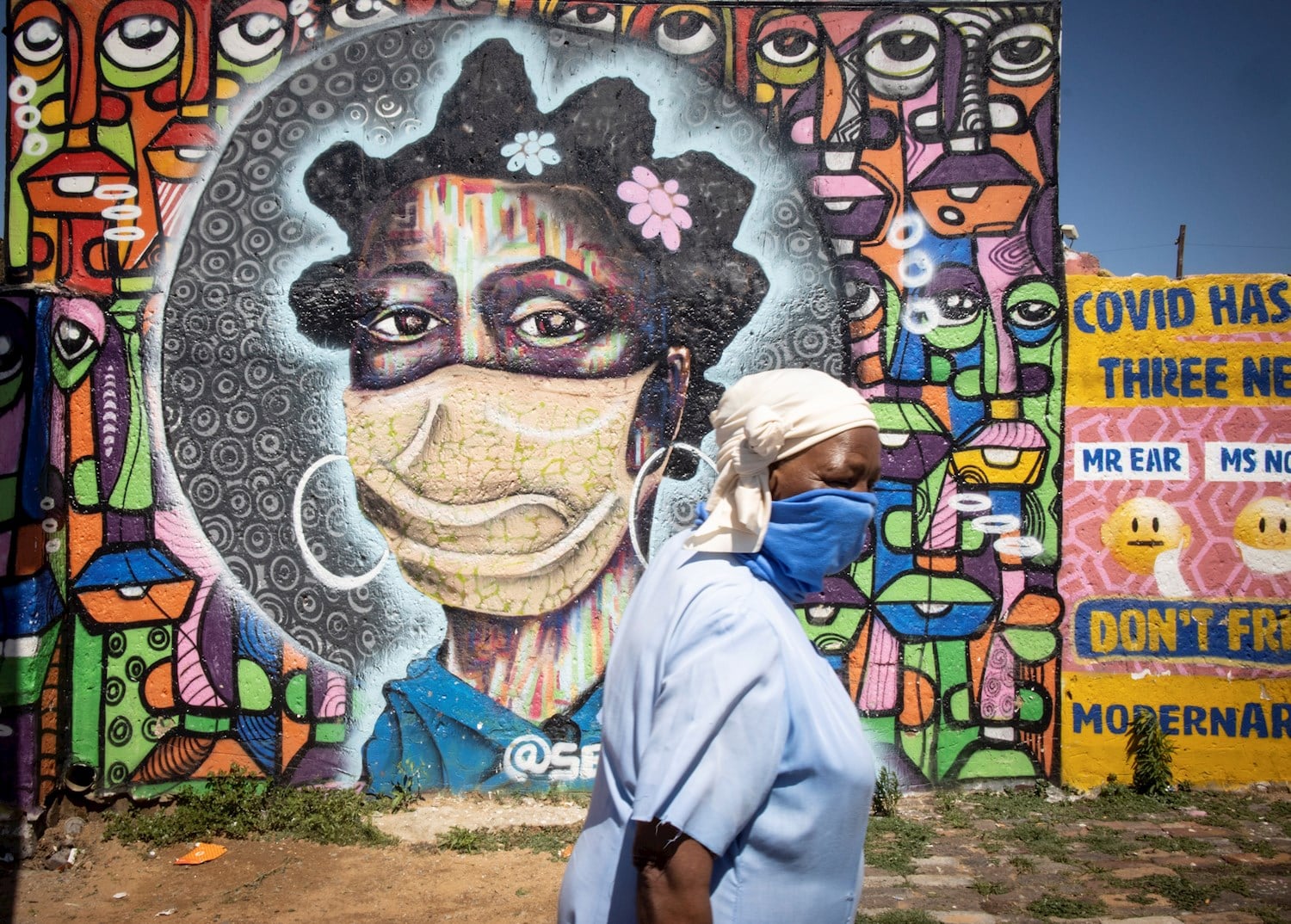Una residente del barrio de Soweto en Johannesburgo, Sudáfrica, pasa delante de un mural que representa a una mujer con una mascarilla