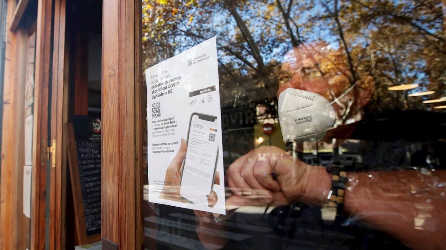 Un empresario coloca un cartel en Cataluña informando de la exigencia del pasaporte covid para acceder al local.