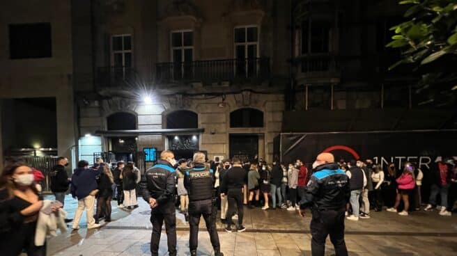 Varios policías locales vigilan a un grupo de jóvenes que guardan en una cola para acceder a un local de ocio nocturno la pasada noche en Vigo.