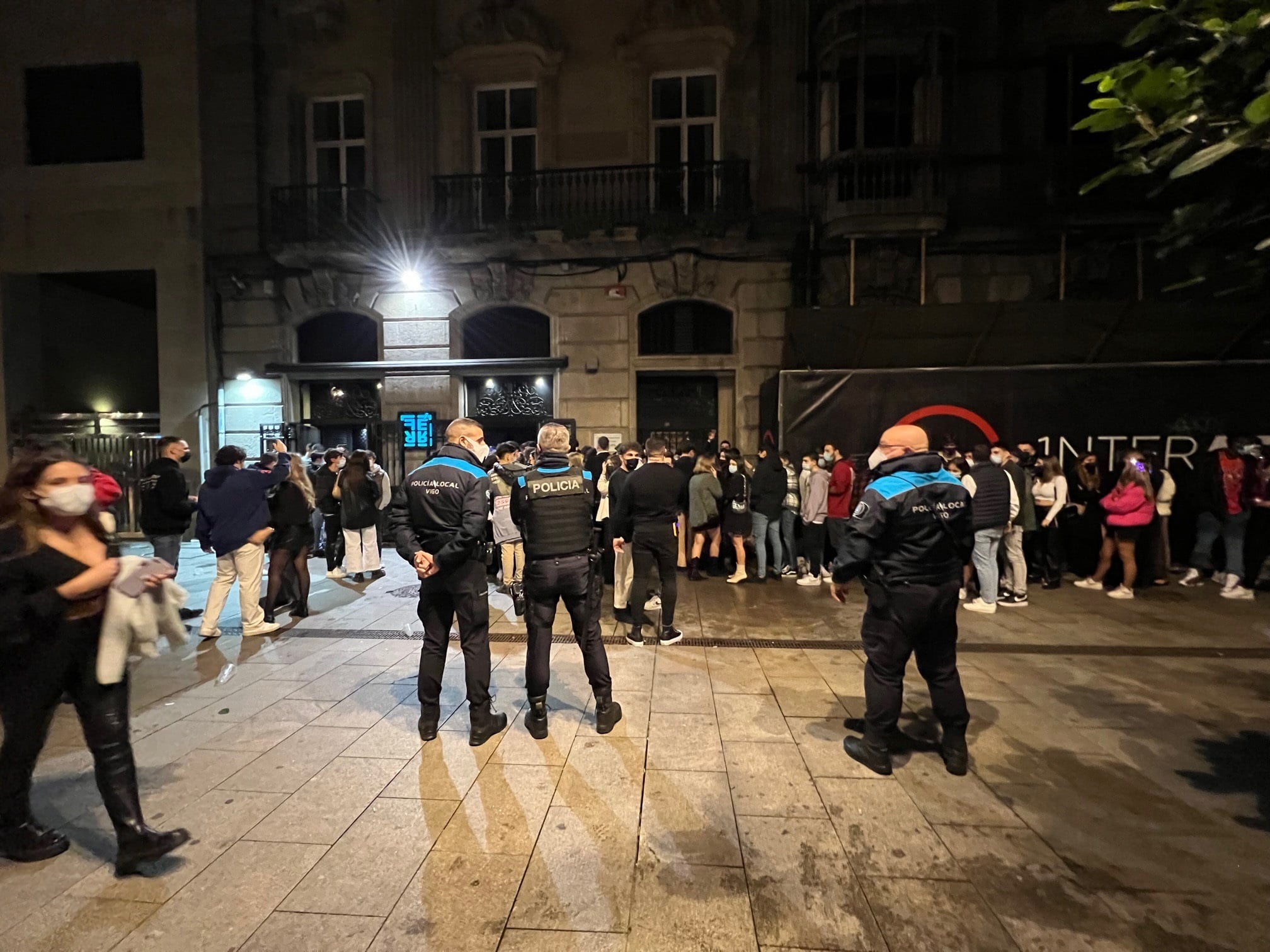 Varios policías locales vigilan a un grupo de jóvenes que guardan en una cola para acceder a un local de ocio nocturno la pasada noche en Vigo.