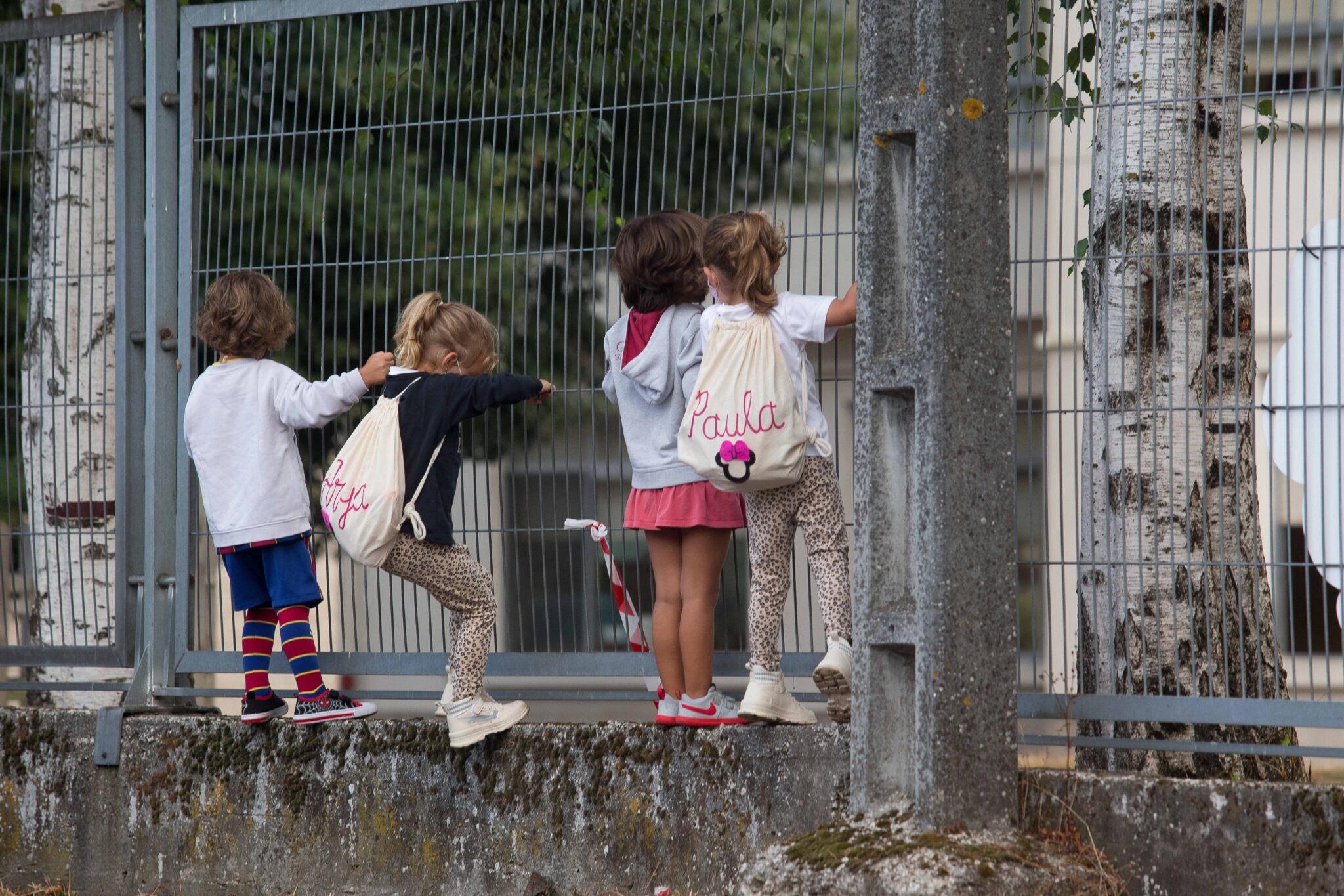 Varios niños y niñas se encaraman a la valla del CEIP Manuel Mallo de Nadela.