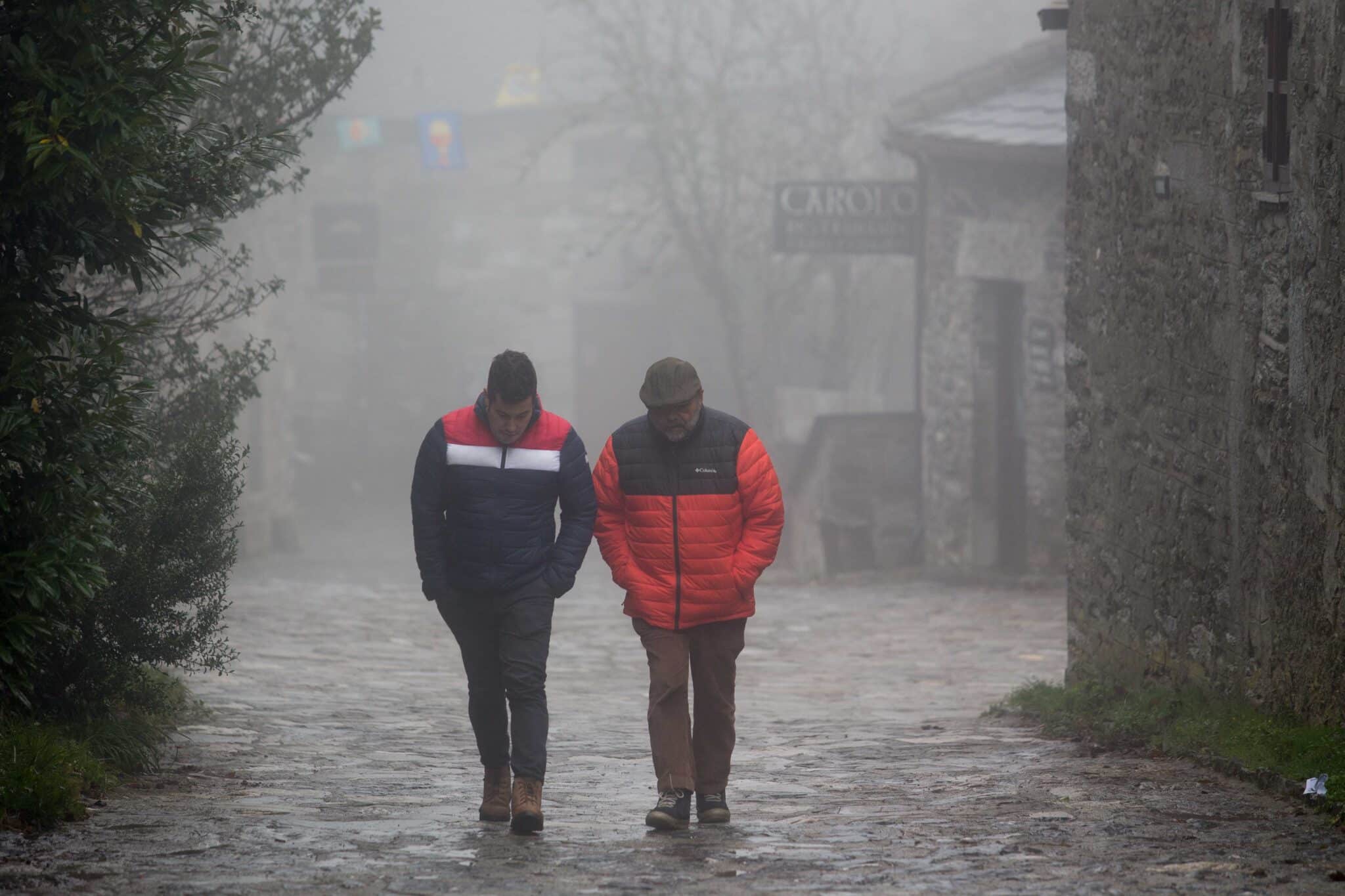 Dos hombres caminan entre la niebla en la aldea prerromana de O Cebreiro, Concello de Pedrafita do Cebreiro, Lugo, Galicia (España)